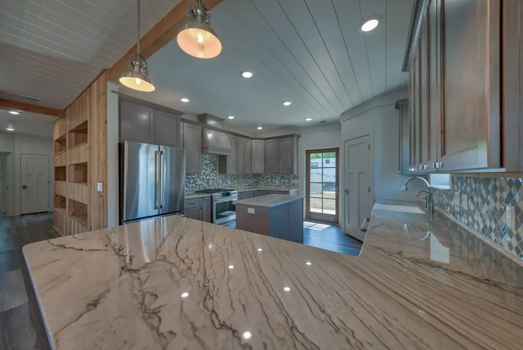 Interior photo of a home built by Harvell Homes in Powell, Wyoming featuring a luxurious custom kitchen with premium appliances, an island, farmhouse kitchen sink, pendants, premium backsplash, and wood-beam and shiplap ceiling