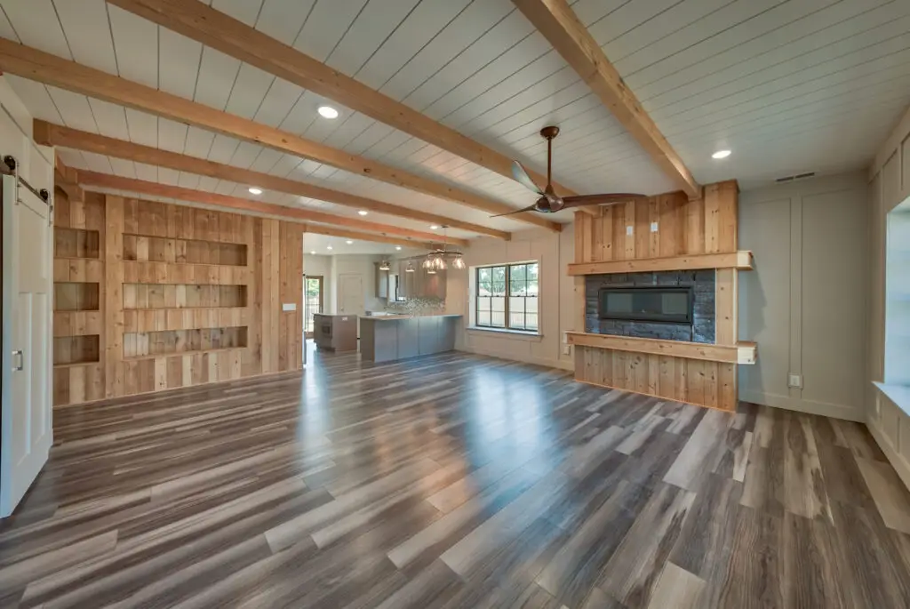 Interior photo of a home built by Harvell Homes in Powell, Wyoming featuring a luxurious custom living room with floor-to-ceiling stone and wood fireplace, wood-beam and shiplap ceiling, and open-floor plan to the kitchen
