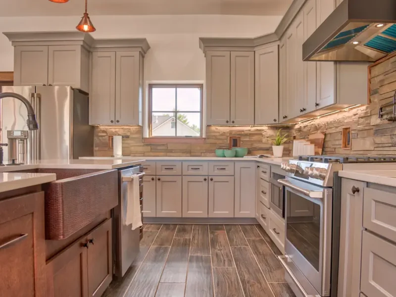 Interior photo of a home built by Harvell Homes in Powell, Wyoming featuring a luxurious custom kitchen with tray ceiling, premium appliances, wood island with premium countertop, wall-mount pot filler faucet, farmhouse kitchen sink, elevated stone backsplash, kitchen hood and wood-look plank tile flooring