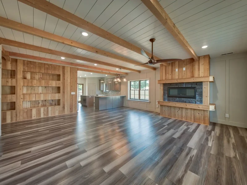 Interior photo of a home built by Harvell Homes in Powell, Wyoming featuring a luxurious custom living room with floor-to-ceiling stone and wood fireplace, wood-beam and shiplap ceiling, and open-floor plan to the kitchen